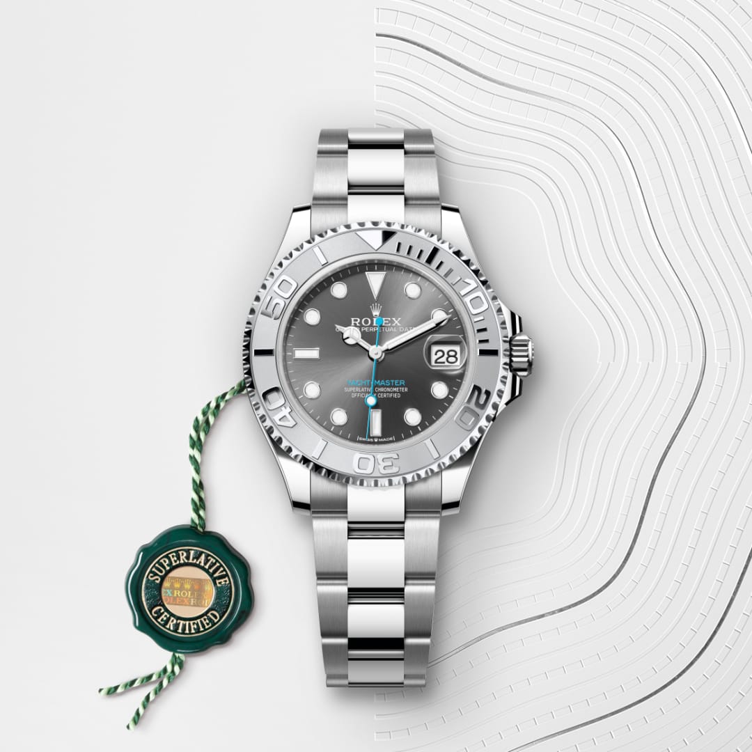 A silver Rolex Yacht-Master watch with a grey dial and date, beside a green Superlative Certified tag.