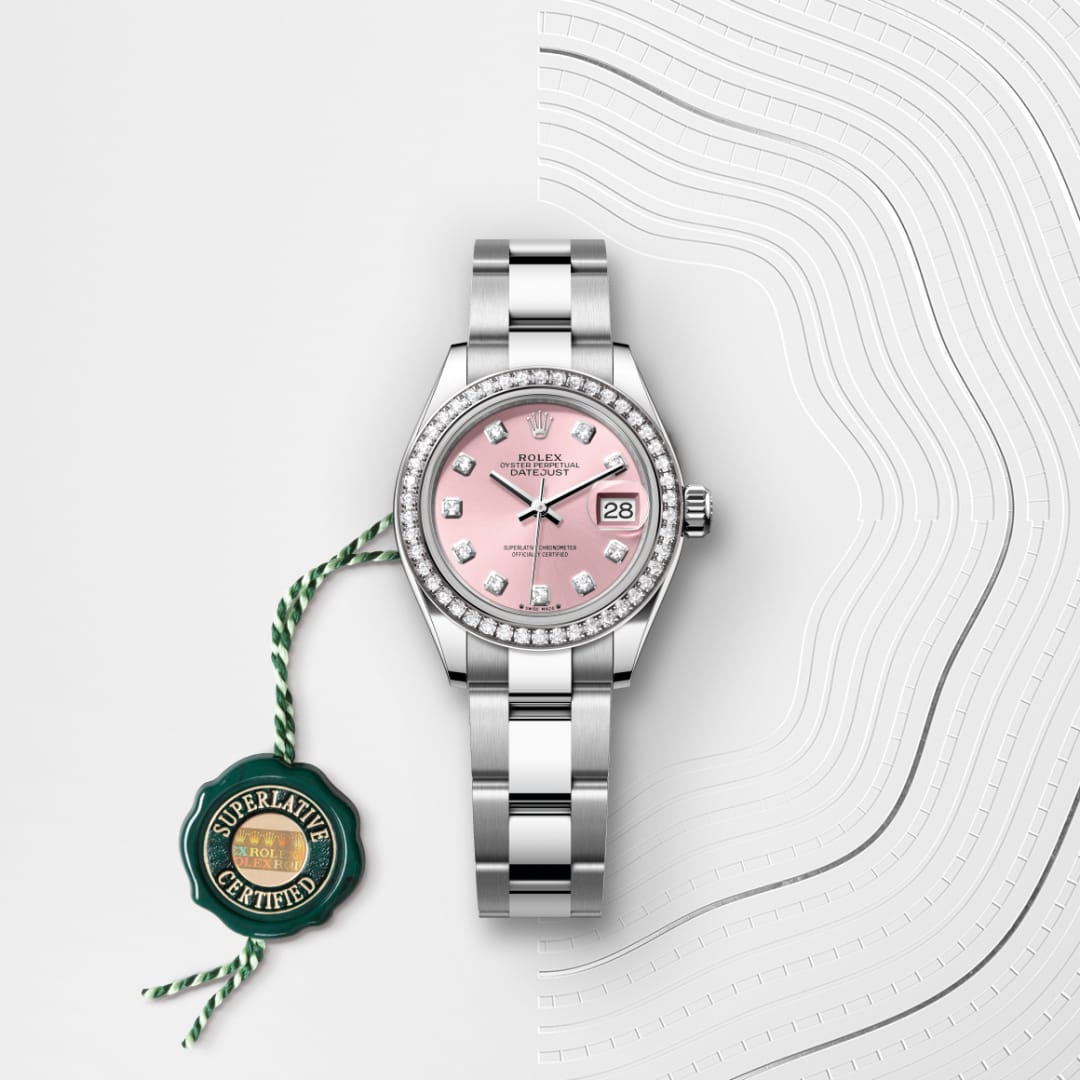 A silver Rolex watch with a pink diamond dial and date display, next to a green Superlative Certified tag.