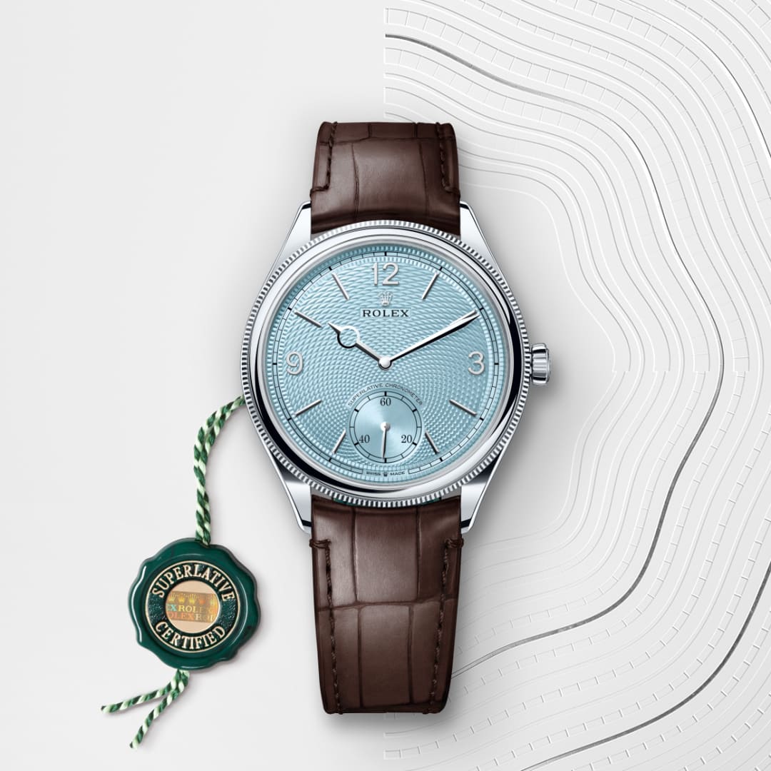 A Rolex watch with a blue face, brown leather strap, and a green “Superlative Certified” tag beside it.