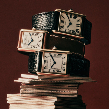Three Cartier watches with leather straps stacked horizontally on some paper cards