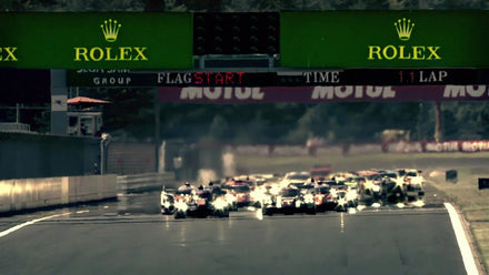 Race cars speed off the starting line under Rolex signage at a professional motorsport event.