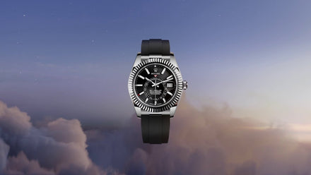 A luxury wristwatch with a black strap and black dial, floating above clouds at sunrise.