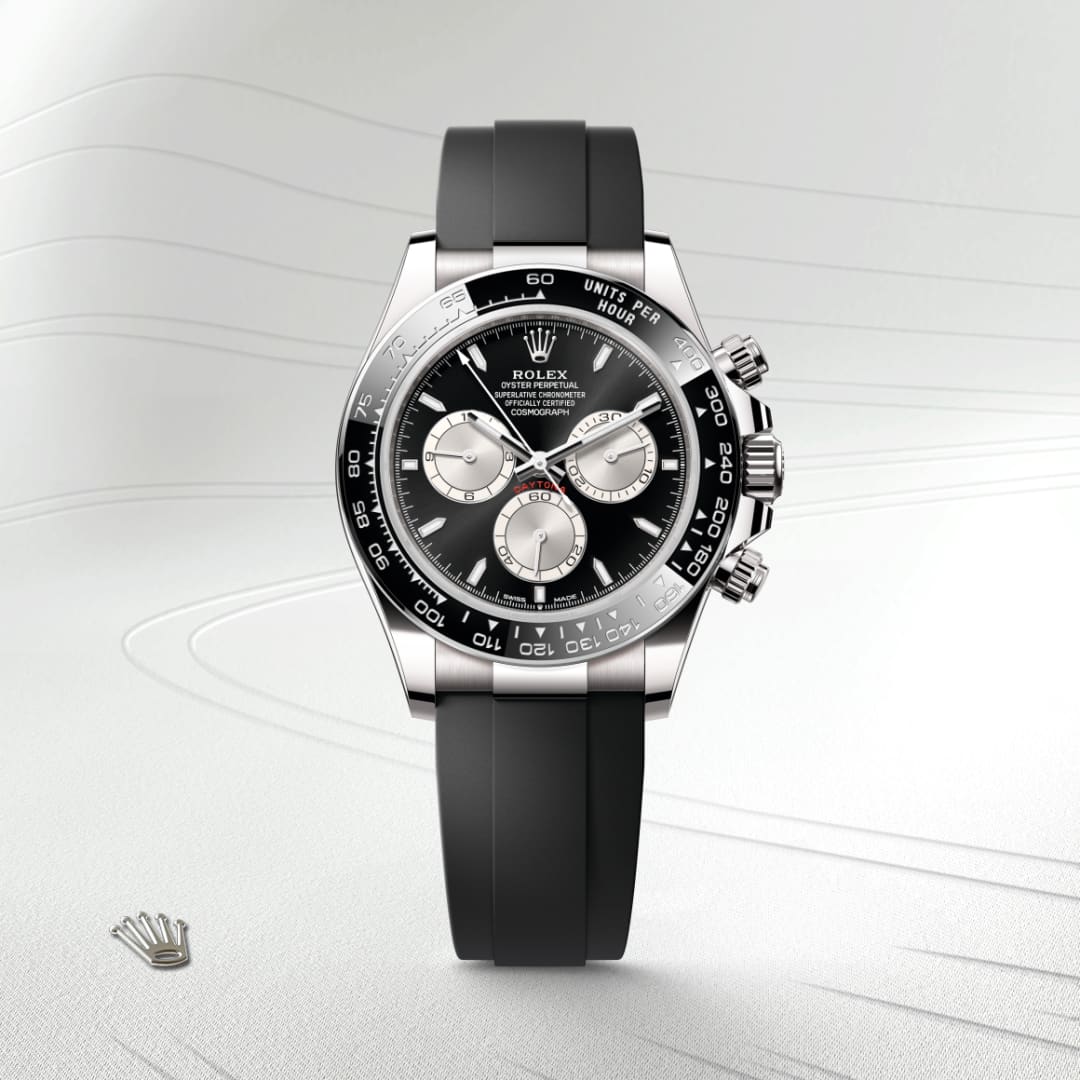 A Rolex Daytona watch with a black dial and black rubber strap displayed on a light textured background.