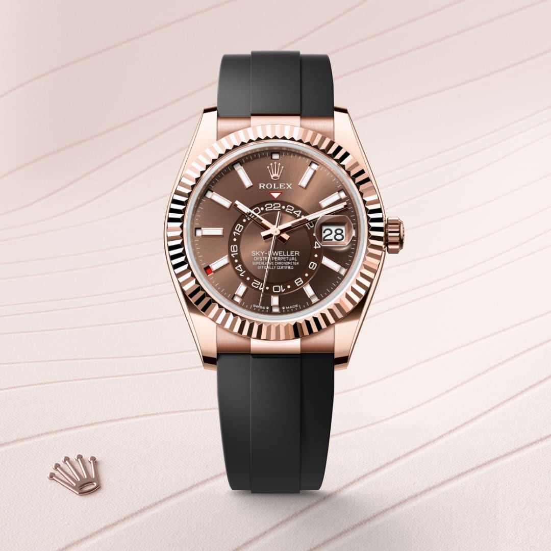 A rose gold Rolex Sky-Dweller with a black strap on a textured light pink background.