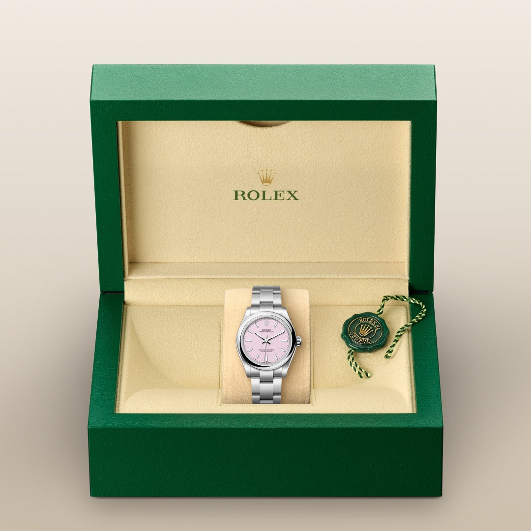 A Rolex watch with a pink dial in a green and beige Rolex box, with a Rolex tag on the right.