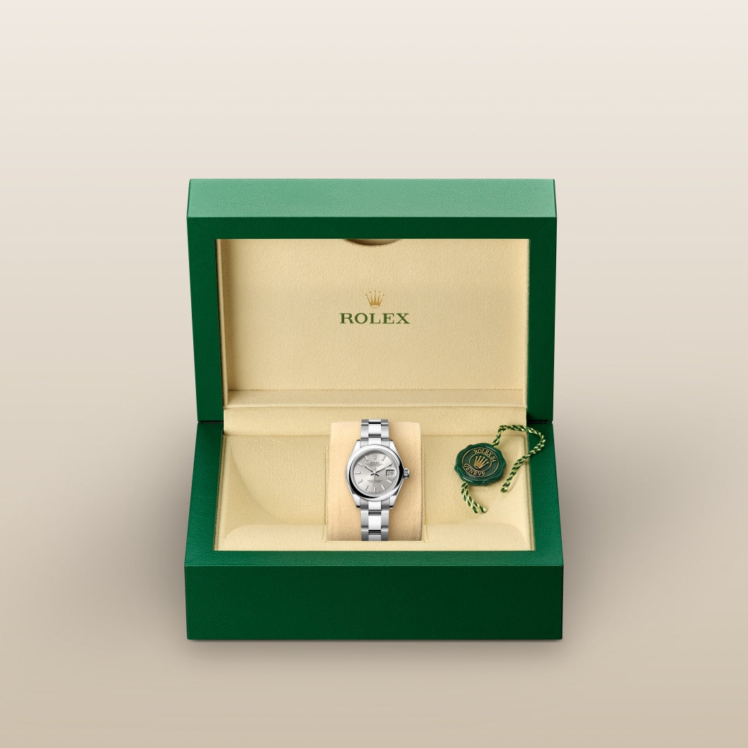 A silver Rolex wristwatch in a green and cream Rolex box with a green and gold tag beside it.