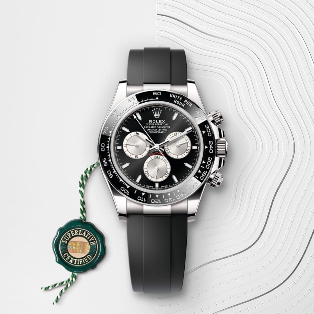 A Rolex Daytona watch with a black band and face, shown with a green Superlative Certified tag.