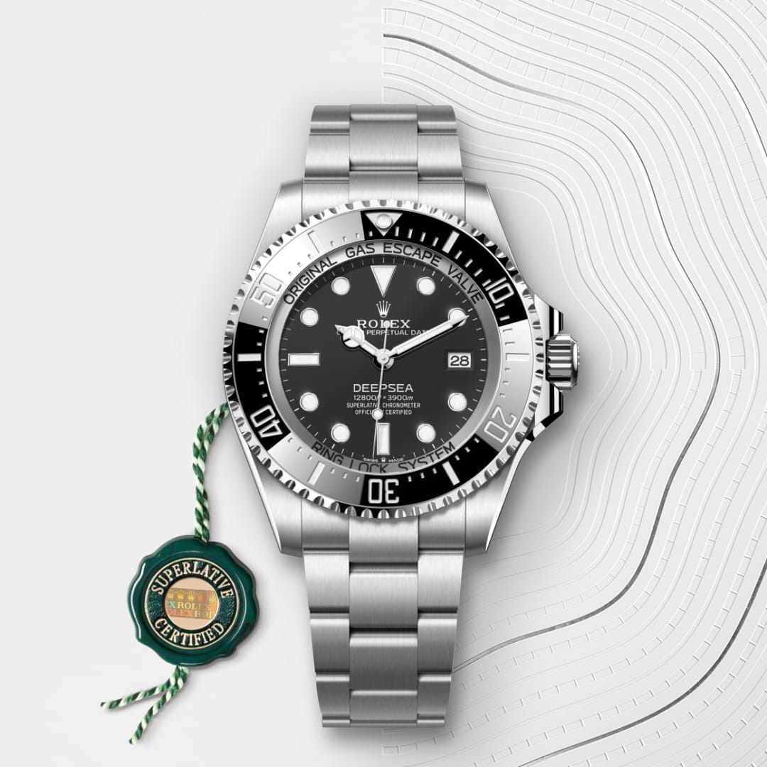 A silver Rolex Deepsea watch with a black dial and bezel, next to a green Superlative Certified tag.
