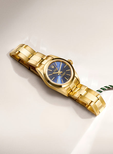 Gold wristwatch with a blue dial and gold hour markers, displayed on a light-colored surface.