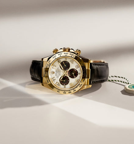 A gold chronograph watch with a white dial and black leather strap, displayed on a light surface.
