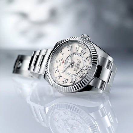A silver Rolex watch with a white dial and Roman numerals is displayed on a reflective surface.