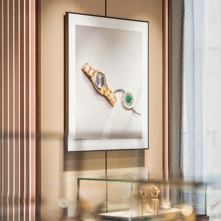 Framed photo of two luxury watches displayed above a glass case with watches inside a jewelry store.