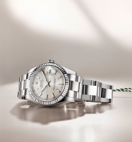 Silver luxury wristwatch with a white dial and metal bracelet, displayed on a smooth, light-colored surface.