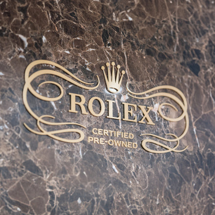 Gold Rolex Certified Pre-Owned logo on a dark, marbled stone background.