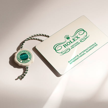 Rolex international guarantee card and green Rolex certified pre-owned tag on a light surface.