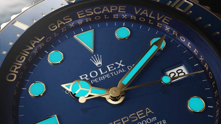 Close-up of a blue Rolex watch face with gold accents and glowing blue hour markers and hands.