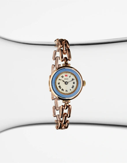 A vintage Bulova gold wristwatch with a blue bezel and Roman numeral dial, displayed on a clear stand.