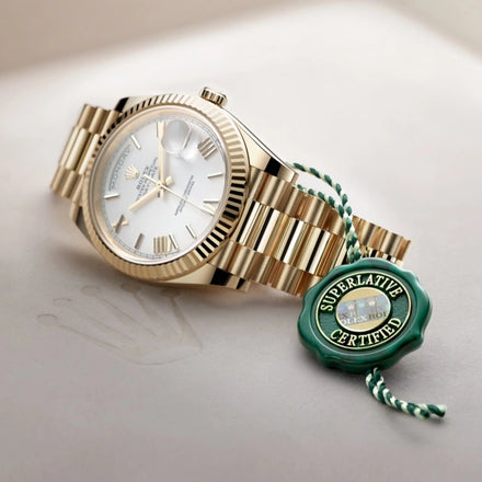 A gold Rolex watch with a white dial beside a green Superlative Certified tag on a beige surface.