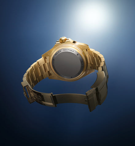 Gold Rolex Deepsea watch with an open clasp, shown from the back against a blue gradient background.