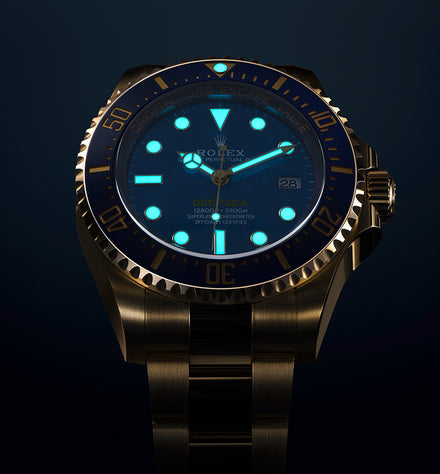A Rolex watch with glowing blue hands and hour markers in a dark setting.