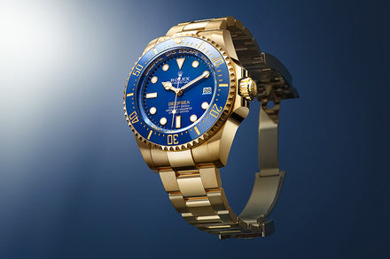 A gold Rolex Deepsea watch with a blue dial and bezel displayed against a blue gradient background.