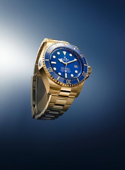 A gold Rolex watch with a blue face and bezel, displayed against a gradient blue background.