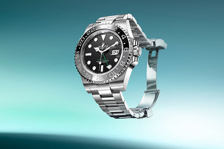 A stainless steel Rolex watch with a black dial and silver bracelet displayed against a gradient teal background.
