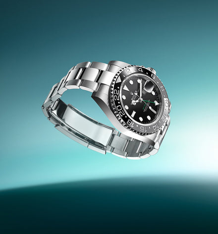 A luxury silver wristwatch with a black dial and metal band, displayed against a gradient teal background.