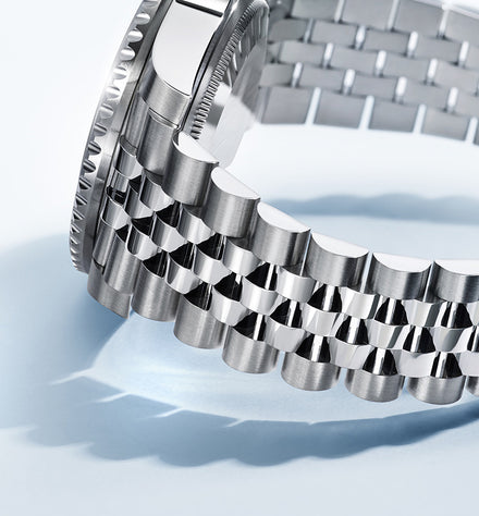 Close-up of a silver metal watch bracelet with polished and brushed links on a light background.