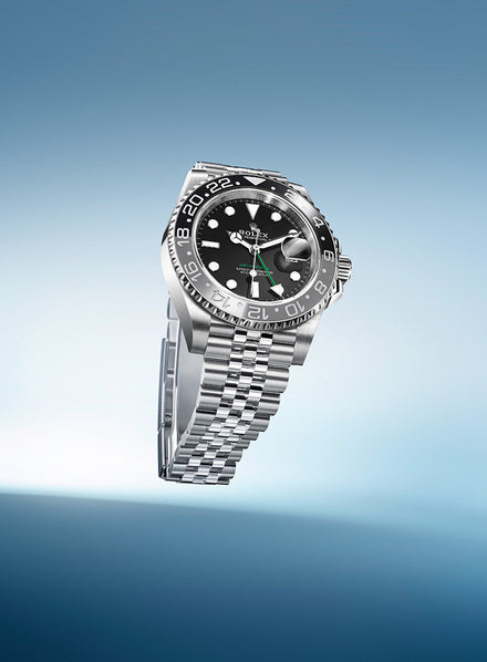 A silver Rolex watch with a black dial and bezel displayed against a gradient blue background.