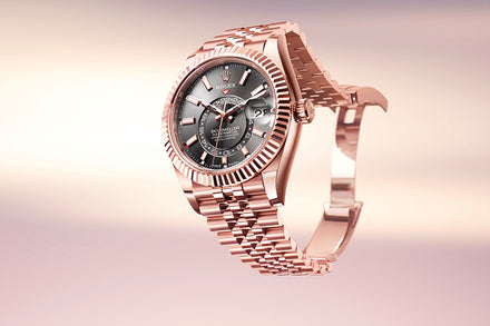 A rose gold Rolex watch with a black dial and fluted bezel, displayed against a soft, gradient background.