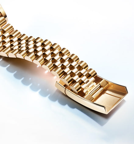 Close-up of a gold metal watch bracelet with a polished, reflective surface and intricate links.