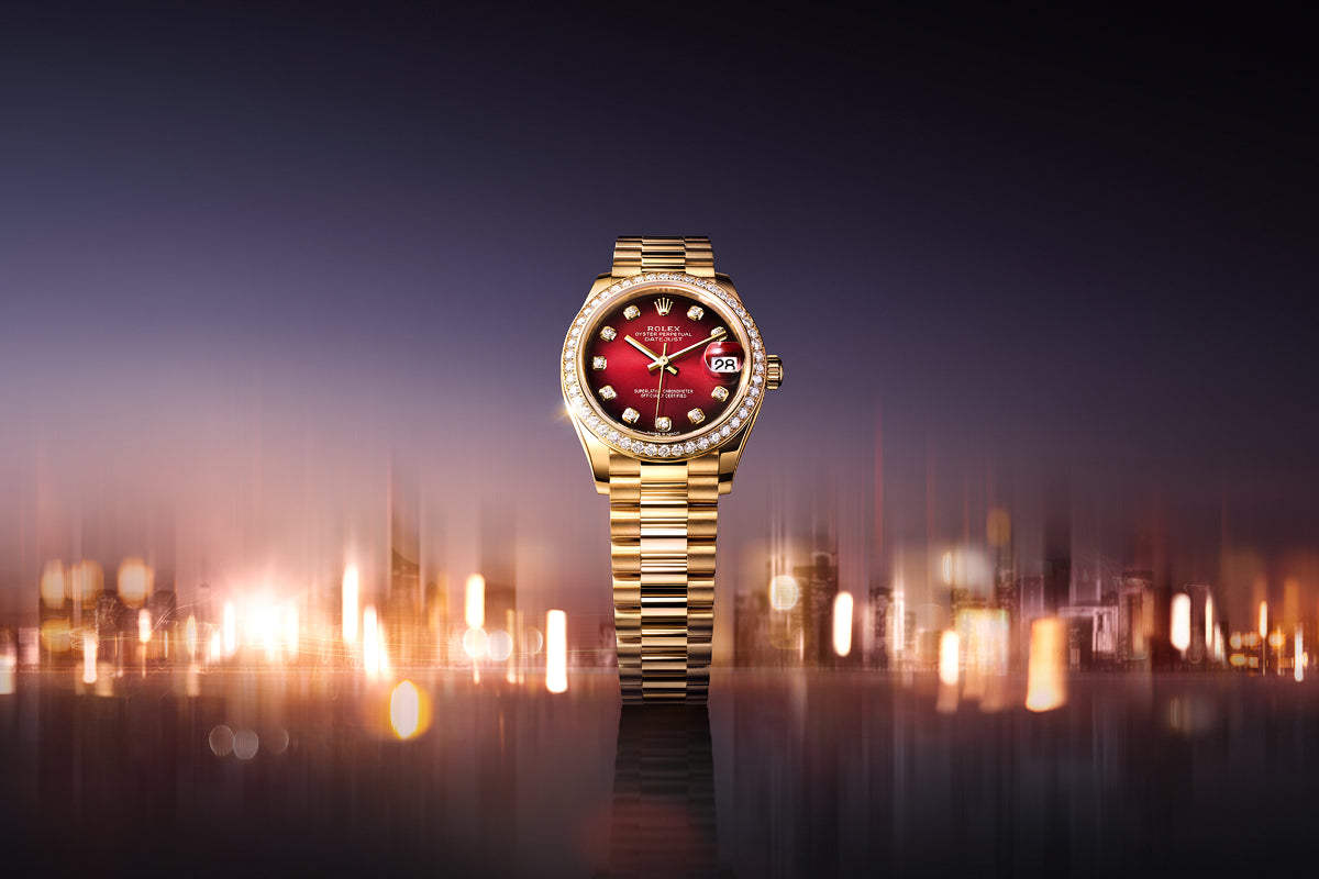 A gold luxury watch with a red face and diamond markers, set against a blurred city lights background.