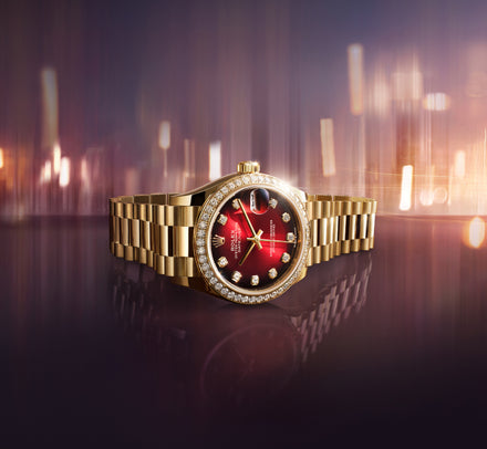 A gold luxury watch with a red face and diamond accents, displayed against a blurred, glowing background.