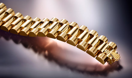 Close-up of a gold watch bracelet with a polished and brushed finish on a reflective surface.