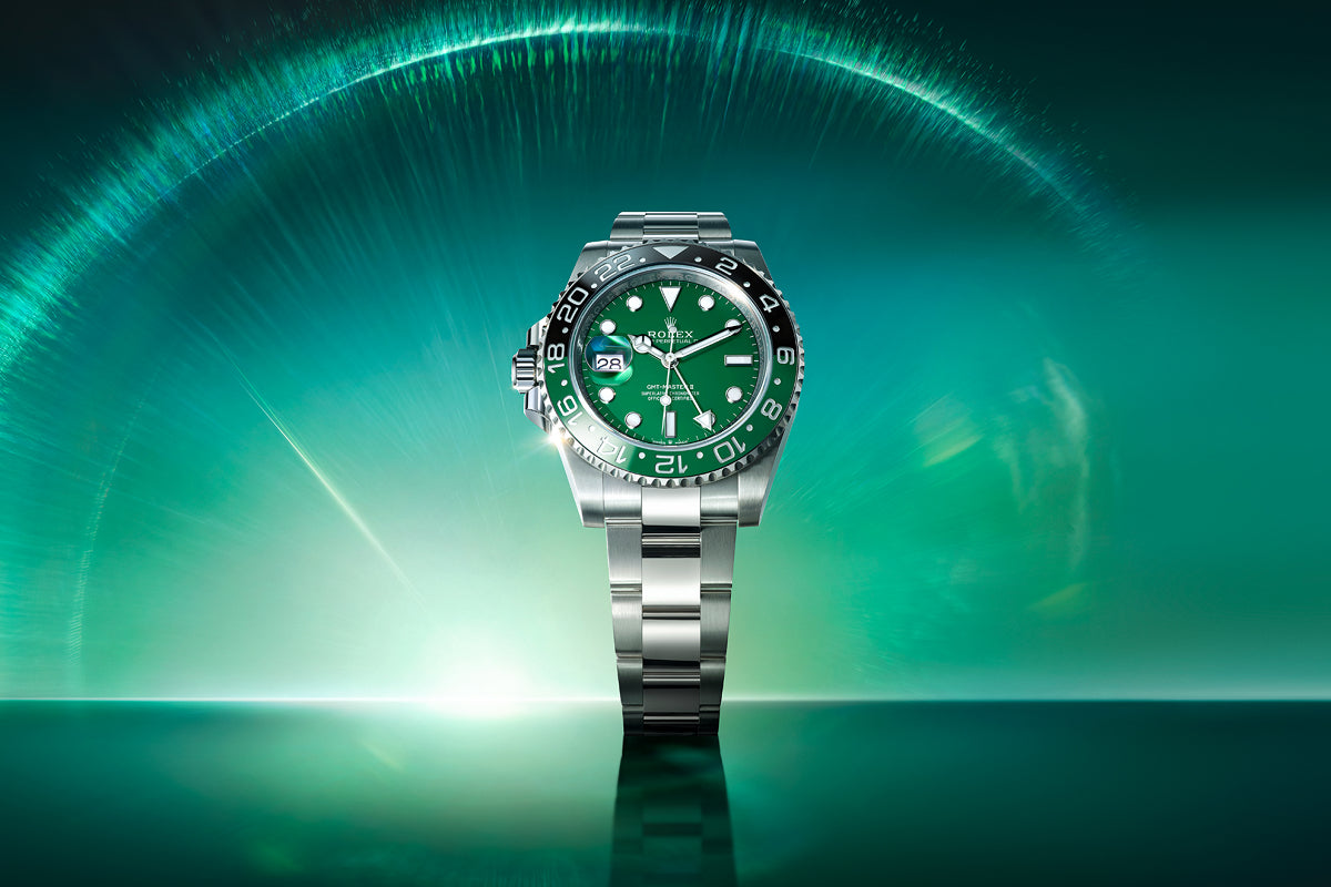 A silver Rolex watch with a green dial and bezel is displayed on a reflective green surface with a glowing background.