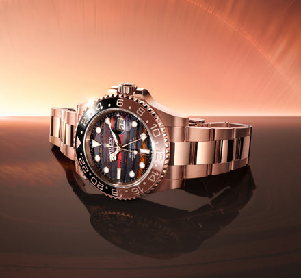 A luxury rose gold watch with a multicolored dial displayed on a shiny, reflective surface with a warm background.