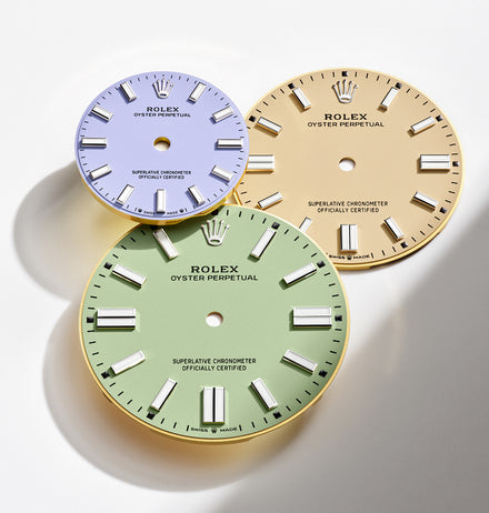 Three Rolex watch dials in pastel purple, yellow, and green colors arranged on a white background.