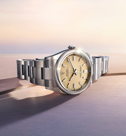 A silver wristwatch with a champagne dial is displayed on a smooth surface under soft sunlight.