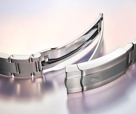 Close-up of a stainless steel watch clasp and bracelet with a Rolex crown logo on a soft gradient background.
