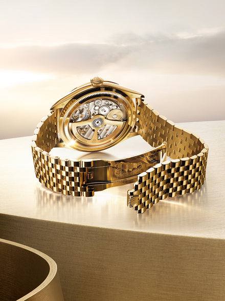 A gold wristwatch with an open clasp, showcasing its intricate internal mechanism, resting on a metallic surface.