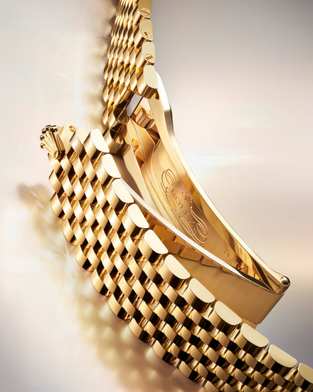 Close-up of a gold watch bracelet and clasp, showing intricate links and detailed engraving inside.