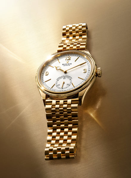 A gold Rolex wristwatch with a white dial on a gold background, reflecting light.