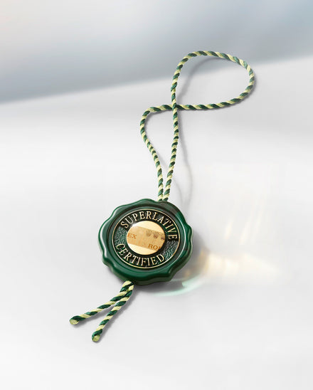 A green and gold Rolex Superlative Certified tag with a twisted green and white string attached.