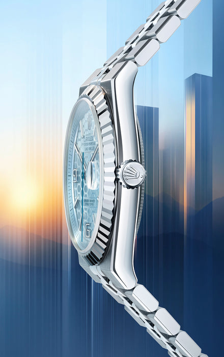 Close-up side view of a silver wristwatch with a blue face against a blurred cityscape at sunrise.