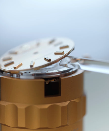 A close-up of watch hands assembling a watch face onto its mechanical movement.