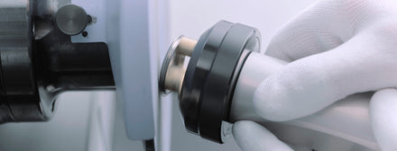 Gloved hand holding a metal tool near a machine for precision work or manufacturing.
