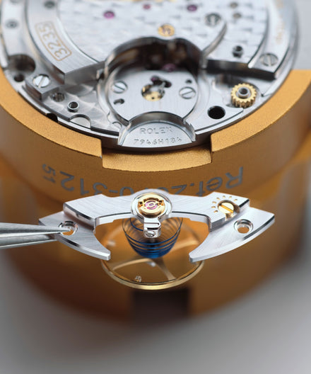 Close-up of a mechanical watch movement being assembled with tweezers, showing intricate inner components.