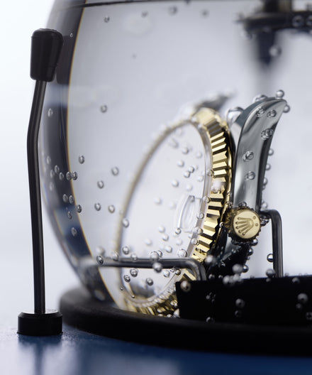 A luxury wristwatch submerged in water with air bubbles clinging to its metal case and crown.