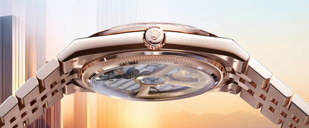 Close-up of a luxury wristwatch showing its intricate transparent back and rose gold case against a soft sky background.